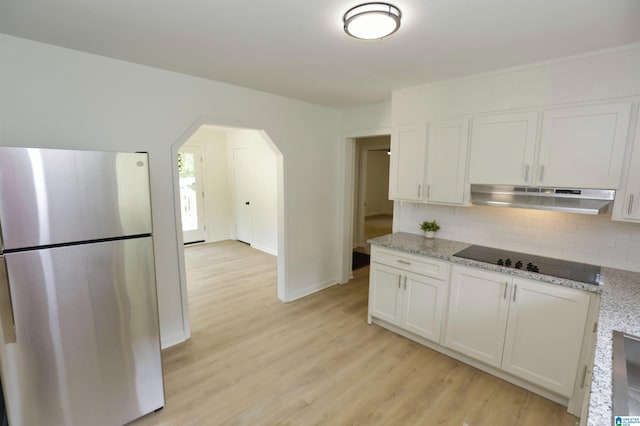 kitchen featuring decorative backsplash, black electric cooktop, white cabinets, freestanding refrigerator, and under cabinet range hood