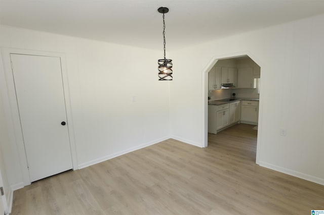 unfurnished dining area with arched walkways, baseboards, and light wood-style floors