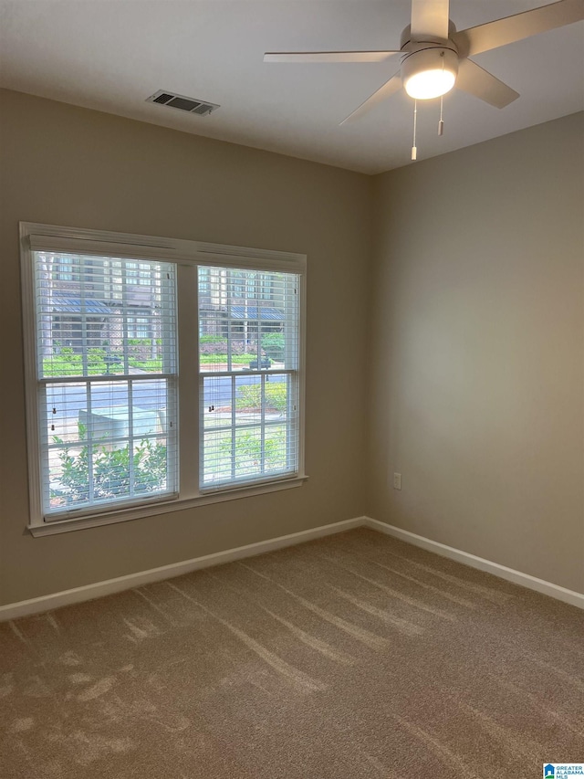 carpeted spare room featuring baseboards, a ceiling fan, and visible vents