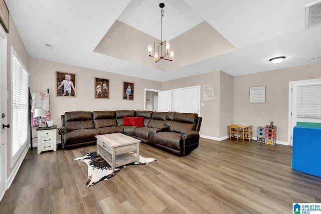 living area featuring baseboards, a healthy amount of sunlight, wood finished floors, a tray ceiling, and visible vents