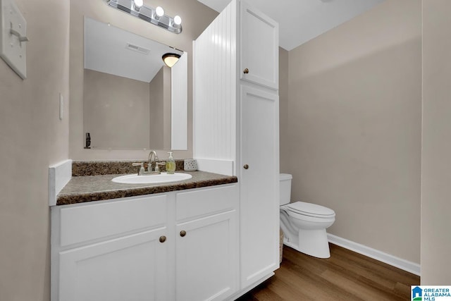 bathroom featuring vanity, toilet, baseboards, wood finished floors, and visible vents