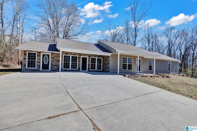 ranch-style home with a porch, a shingled roof, stone siding, and concrete driveway