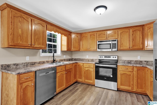 kitchen with a sink, appliances with stainless steel finishes, light wood-style floors, and brown cabinetry