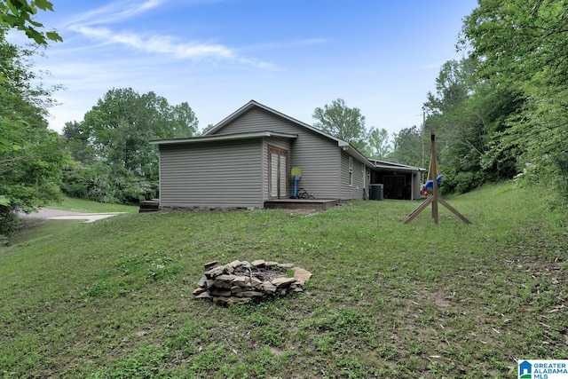 view of side of home featuring a lawn, central air condition unit, and a fire pit