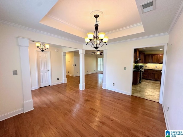 unfurnished dining area featuring an inviting chandelier, a tray ceiling, ornate columns, and visible vents
