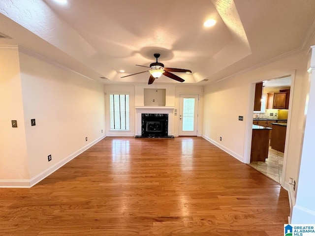 unfurnished living room featuring wood finished floors, baseboards, ceiling fan, recessed lighting, and a tray ceiling