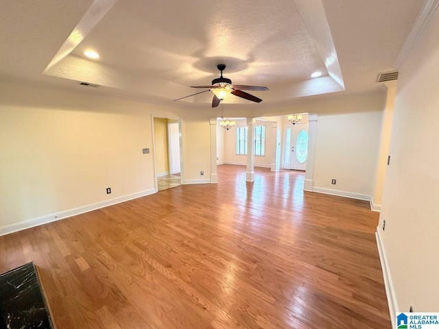 unfurnished room with a raised ceiling, ceiling fan with notable chandelier, light wood finished floors, and visible vents