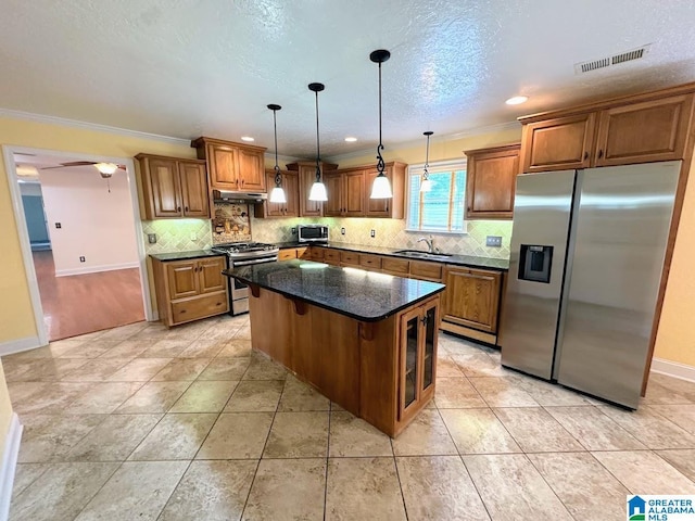 kitchen featuring visible vents, brown cabinetry, crown molding, under cabinet range hood, and stainless steel appliances