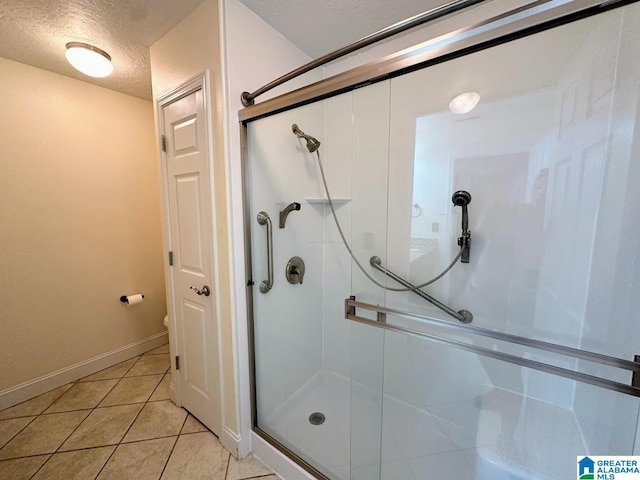 full bathroom featuring a textured ceiling, tile patterned floors, a shower stall, and baseboards