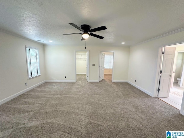 unfurnished bedroom with crown molding, baseboards, a walk in closet, and light carpet