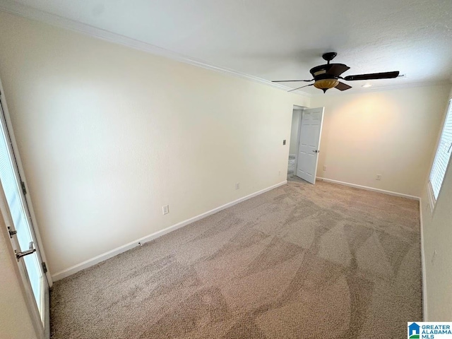carpeted empty room featuring baseboards, ornamental molding, and a ceiling fan