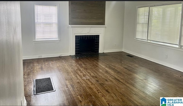 unfurnished living room with a tiled fireplace, a wealth of natural light, wood finished floors, and visible vents
