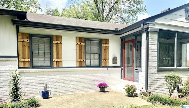 view of exterior entry with brick siding and a shingled roof