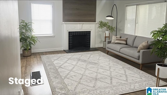 living area with baseboards, visible vents, a tiled fireplace, and wood finished floors