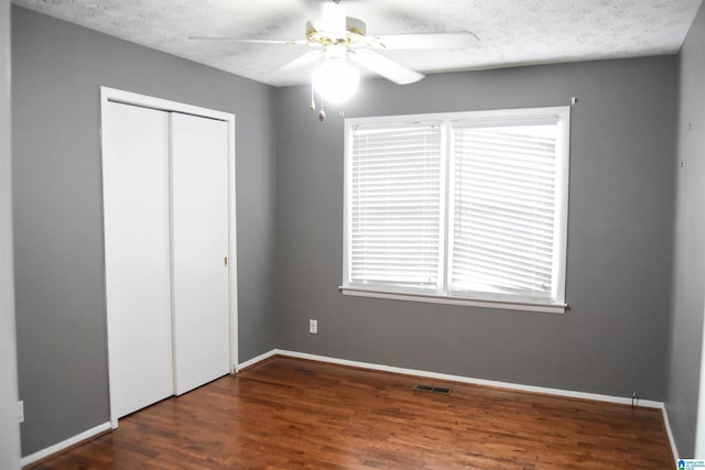 unfurnished bedroom with ceiling fan, visible vents, wood finished floors, baseboards, and a closet