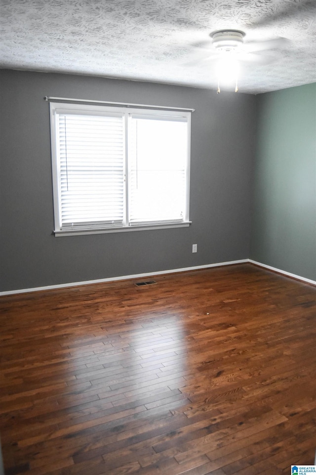 empty room with visible vents, a textured ceiling, a healthy amount of sunlight, and dark wood-style floors