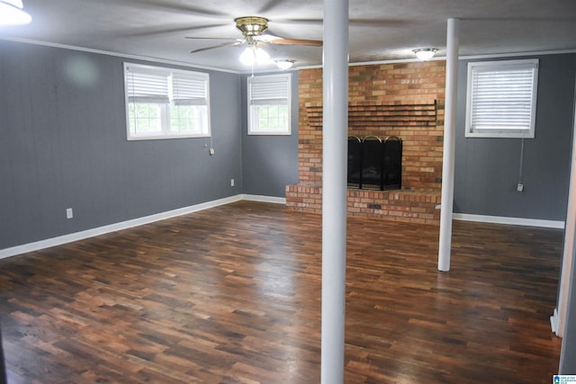 below grade area with a brick fireplace, dark wood finished floors, a ceiling fan, baseboards, and ornamental molding