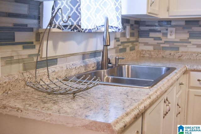 kitchen with a sink, white cabinets, and backsplash