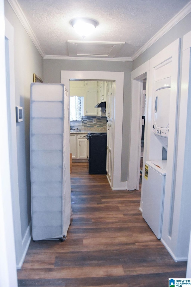 hallway with crown molding, dark wood-style flooring, stacked washer / drying machine, a textured ceiling, and baseboards