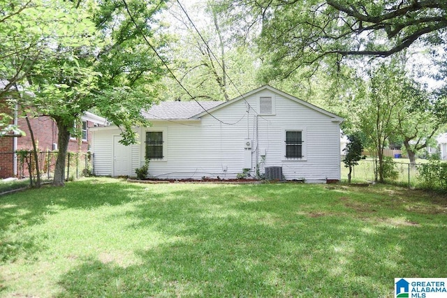 rear view of property featuring central air condition unit, a shingled roof, fence, and a yard