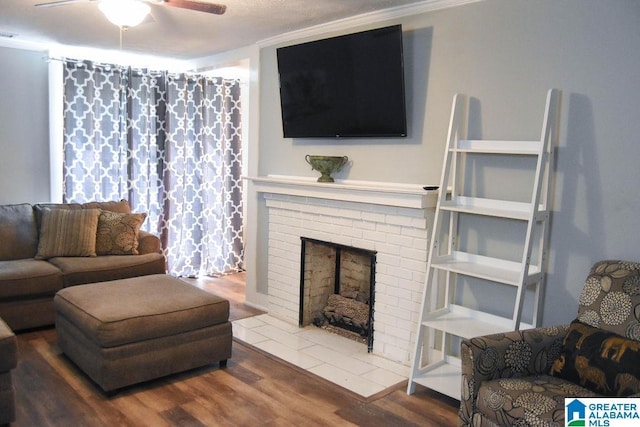 living area with a fireplace, a ceiling fan, and wood finished floors