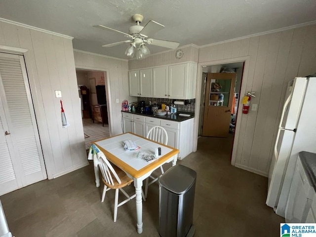 kitchen with crown molding, freestanding refrigerator, dark countertops, white cabinets, and a ceiling fan