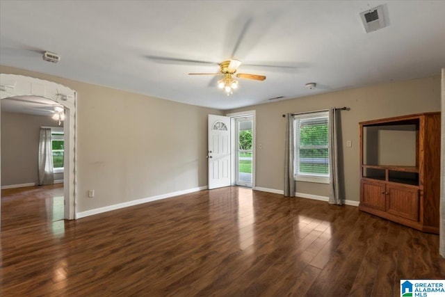 unfurnished room with dark wood-style flooring, a ceiling fan, arched walkways, and baseboards