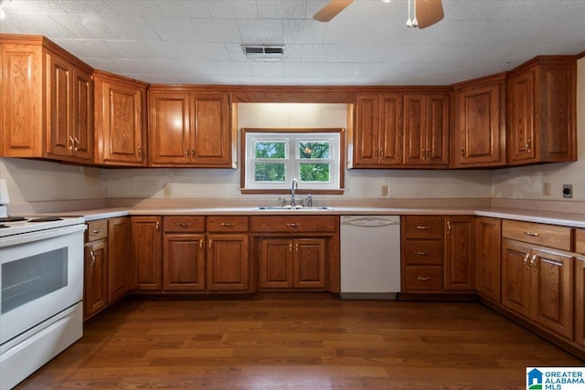 kitchen featuring brown cabinets, dark wood finished floors, a sink, light countertops, and white appliances