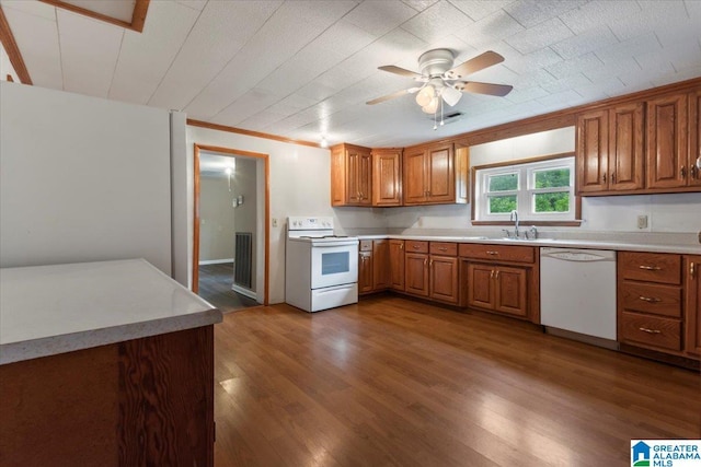 kitchen with brown cabinetry, wood finished floors, white appliances, light countertops, and a sink