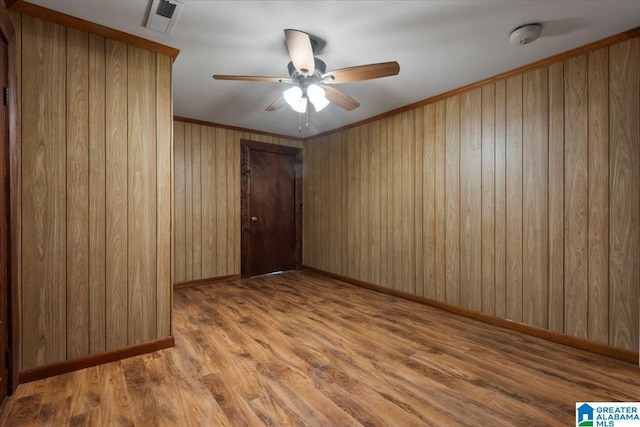 empty room featuring a ceiling fan, visible vents, wood walls, wood finished floors, and baseboards