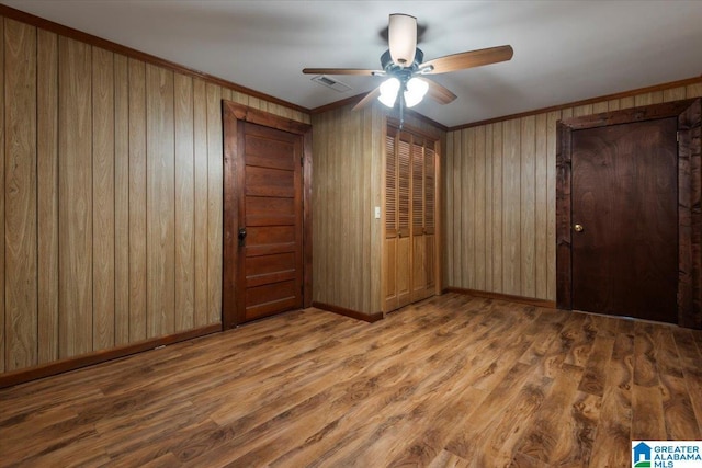 unfurnished bedroom featuring baseboards, ornamental molding, wood finished floors, and wooden walls