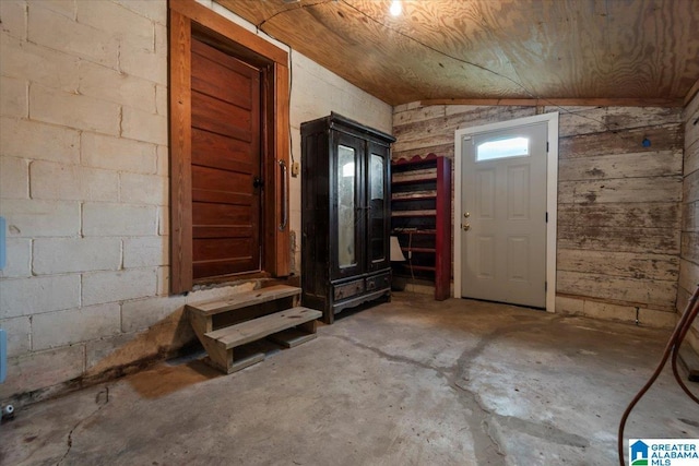 entrance foyer with wood walls, concrete floors, and vaulted ceiling