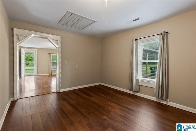 unfurnished room with dark wood-type flooring, attic access, baseboards, and visible vents