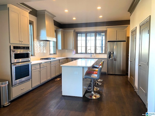 kitchen featuring wall chimney range hood, a kitchen breakfast bar, appliances with stainless steel finishes, light countertops, and ornamental molding