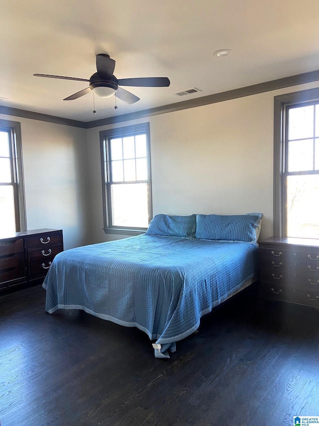 bedroom with ceiling fan, multiple windows, wood finished floors, and visible vents