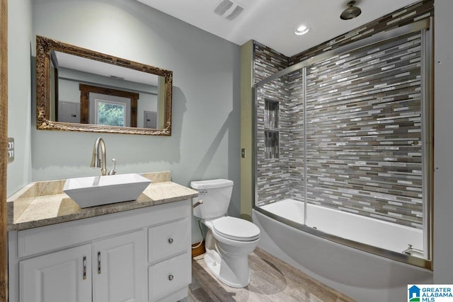 full bath with visible vents, vanity, wood finished floors, toilet, and combined bath / shower with glass door