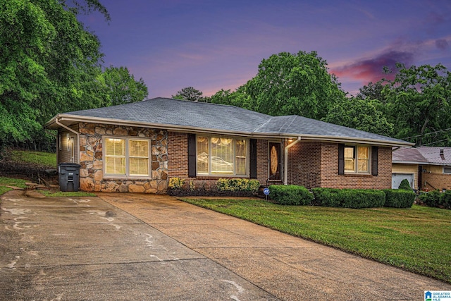 ranch-style house with a yard, driveway, a shingled roof, and stone siding