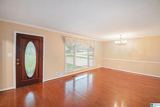 foyer entrance with visible vents, crown molding, an inviting chandelier, wood finished floors, and a textured ceiling