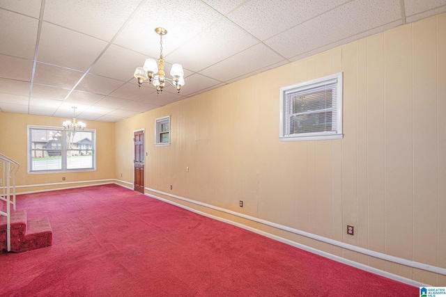 below grade area featuring an inviting chandelier, baseboards, carpet, and a drop ceiling