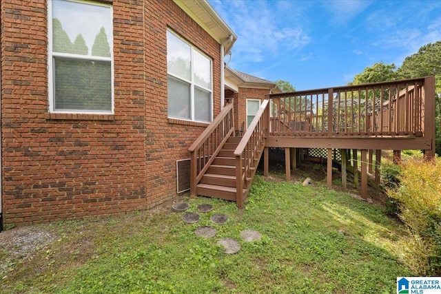 rear view of house featuring brick siding, a deck, stairs, and a yard