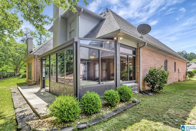 rear view of house with brick siding, a lawn, a chimney, and a sunroom