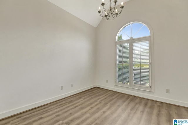 spare room featuring an inviting chandelier, baseboards, wood finished floors, and high vaulted ceiling