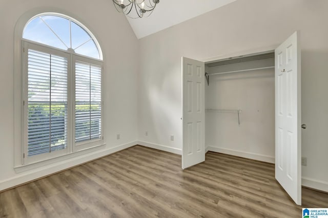 unfurnished bedroom featuring a chandelier, wood finished floors, baseboards, a closet, and lofted ceiling