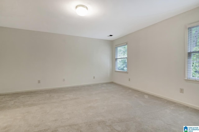 unfurnished room with a healthy amount of sunlight, baseboards, light carpet, and visible vents