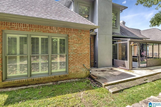exterior space with a shingled roof, a sunroom, and brick siding