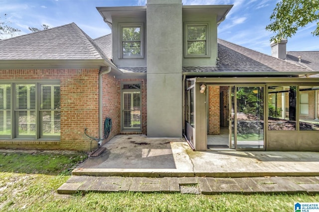rear view of property featuring a patio, a shingled roof, brick siding, and a chimney