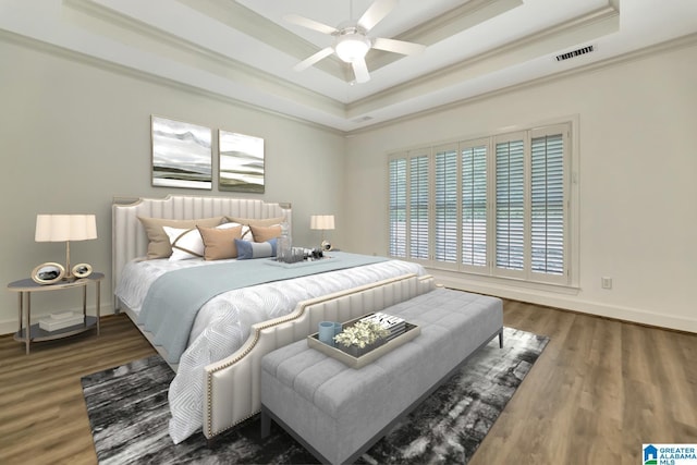 bedroom with wood finished floors, visible vents, baseboards, a raised ceiling, and ornamental molding