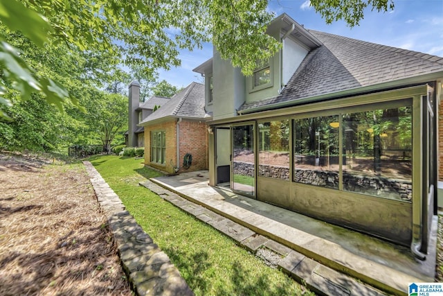back of house featuring roof with shingles, a patio area, brick siding, a yard, and stucco siding