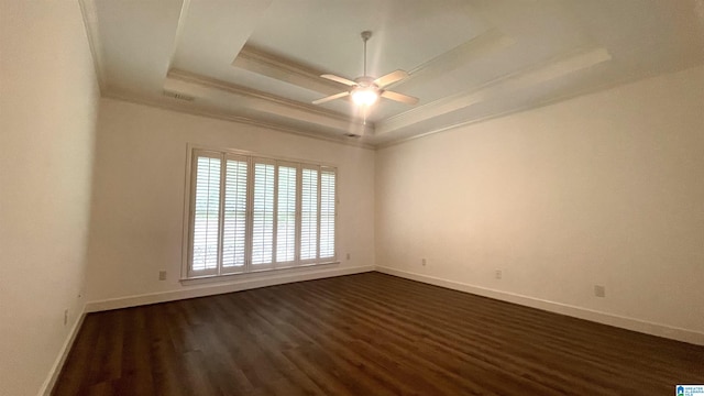 empty room with crown molding, a raised ceiling, ceiling fan, and dark wood finished floors