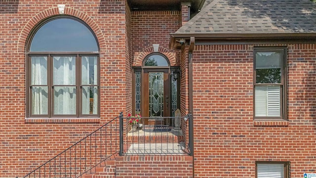 doorway to property featuring brick siding and a shingled roof